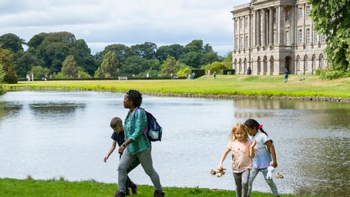 A family walk beside the lake on a sunny spring day with the South front of the house in the background